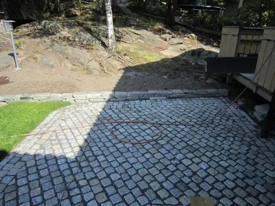 En liten brosteinsbelagt uteplass omgitt av gress og berg.