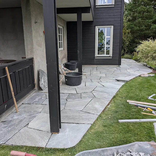 Steinlagt inngangsparti med søyler og grå fliser, foran en bolig.